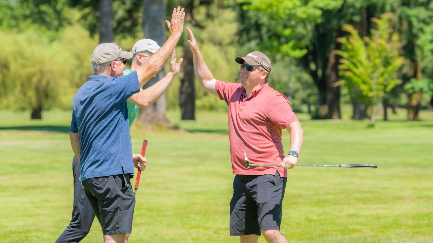 Ryan Stanbery smiles and high-fives Mark McHugh and Craig Kline during a charity golf tournament at Riverside Golf Course in Chehalis on Friday after making a put.